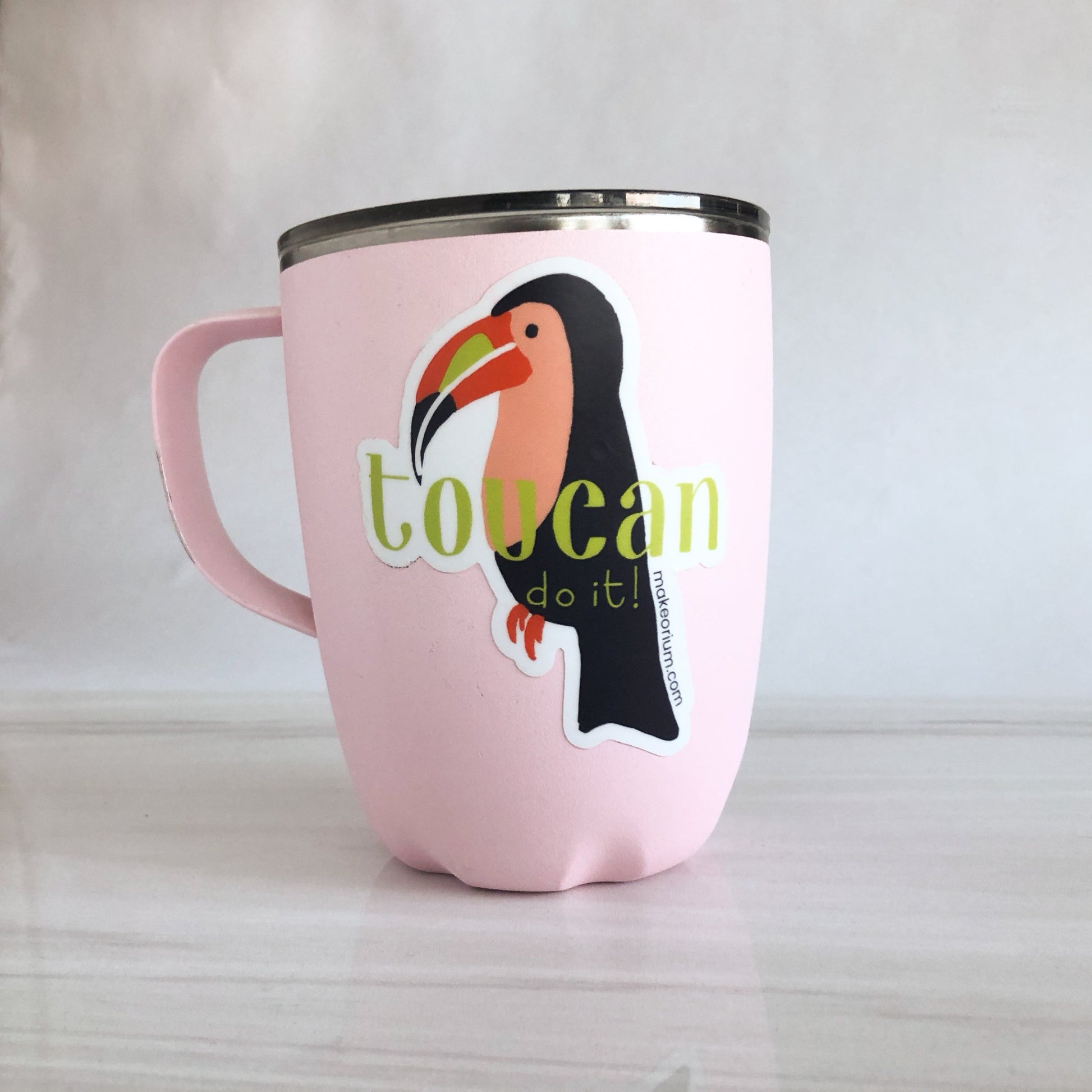 Pink metal mug featuring a vinyl sticker of an illustrated toucan with hand-drawn lettering "Toucan do it!" over the toucan.